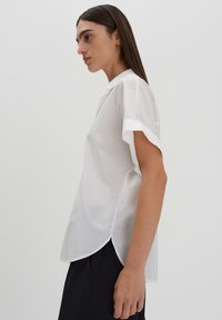 Camicia bianca a maniche corte con colletto, caratterizzata da una vestibilità dritta e orlo curvo. Realizzata in tessuto leggero, design minimalista.