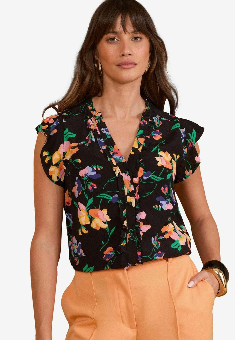 Blouse noire à motifs floraux colorés, avec des manches volantées et un design à boutonnière. Associée à un pantalon pêche taille haute.