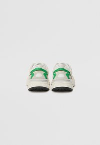 Sneakers bianchi con dettagli verdi, caratterizzati da una suola spessa, collo imbottito e tessuto strutturato. Vista posteriore che mostra i dettagli del marchio.