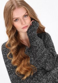 Szürke, textúrált kötött pulóver hosszú ujjakkal. A fonal sötét és világos szálak keverékéből készült, ami réteges megjelenést kölcsönöz.