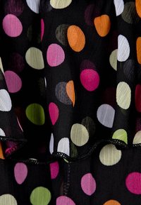 Schwarzer Stoff mit großen, bunten Punkten in Pink, Orange, Weiß, Grün und Flieder. Fließendes Design mit einem Rüschenrand.