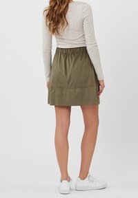 Jupe en suede verte avec taille élastique, de longueur genou, présentant une texture lisse et un design simple. Portée avec des baskets blanches.