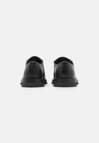 Scarpe in pelle nera con una superficie liscia, forma arrotondata e suola piatta in gomma. Presentano dettagli minimi e un design classico.