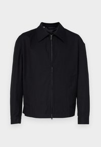 Črna jakna iz gladkega blaga, z zadrgo spredaj, s koničastim ovratnikom in dvema stranskima žepoma.