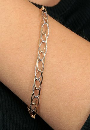 Gold- und Silberkette mit einem Armband, das abwechselnd polierte und strukturierte ovale Glieder zeigt und auf einem hellen Hautton-Handgelenk ruht.