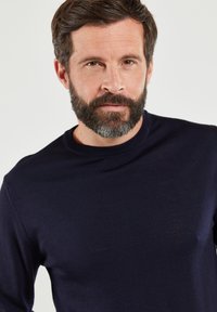 Marineblauwe crew neck trui gemaakt van een zachte, gebreide stof. Slim fit ontwerp met lange mouwen en subtiele geribbelde accenten bij de halslijn.