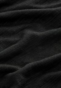 Černá texturovaná tkanina s měkkým, mírně nerovným povrchem. Materiál vypadá lehce a jemně splývá, přičemž odhaluje jemné variace ve stínování.