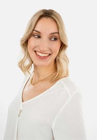 Weiße Bluse mit V-Ausschnitt und drei Knöpfen, die eine glatte Textur aufweist. Getragen mit einer zarten goldenen Kettenkette.