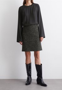 Blusa nera a maniche lunghe con scollatura rotonda abbinata a una gonna grigia testurizzata fino al ginocchio. Indossata con stivali neri alti fino al ginocchio.