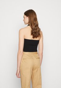 Top halter em malha preta, combinado com calças beje de cintura alta, com detalhes em bolsos traseiros e uma textura suave.