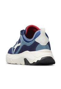 Baskets en suede bleu et marine avec semelle blanche, doublure intérieure rouge et languette blanche au talon, vue en angle depuis le côté arrière droit.