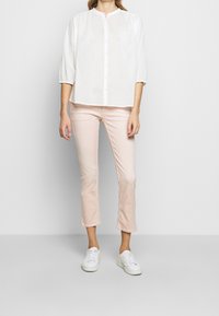 Blouse blanche à boutons avec un col rond et des manches trois-quarts, associée à un jean rose clair court et des baskets blanches.