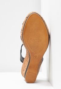 Sandale compensée avec une semelle en liège et un dessus texturé noir. Présente un design ouvert et un léger talon, avec des marquages de la marque sur la semelle.