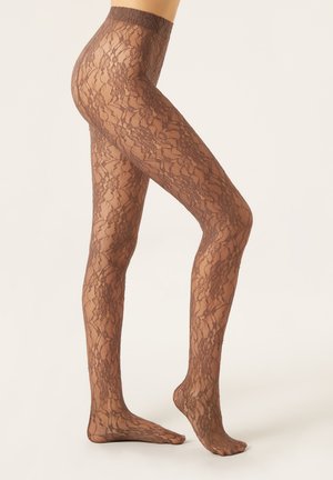 Femme portant des collants en dentelle marron transparent, se tenant sur la pointe des pieds avec un pied à plat et l'autre légèrement levé.
