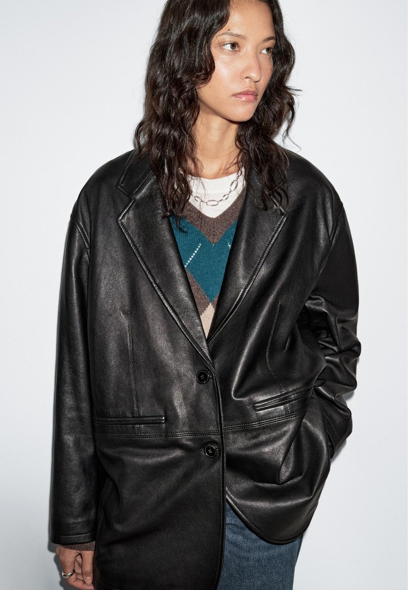 Zwart leren blazer met gekraagde revers, twee voork Generation Xs, een enkele knoopsluiting en een relaxed fit; gedragen over een gebreid patroontrui.