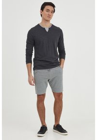 Camisa gris de manga larga superpuesta sobre un corto gris con cintura elástica y cordón; combinado con zapatillas negras. Textura lisa, sin patrones.