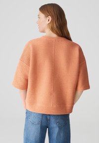 Top corto arancione con texture, maniche corte e scollatura tonda, con cucitura verticale sul retro, abbinato a jeans blu in un taglio rilassato.