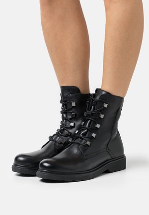 Botas de tobillo de cuero negro con punta redonda, cierre de cremallera y acentos decorativos de hardware cuadrado en los cordones. Suela de goma para tracción.