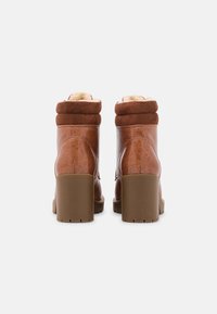 Botas de tobillo de imitación de cuero marrón con un acabado texturizado, puño de tela suave y un tacón grueso beige. Forradas para mayor comodidad y calidez.