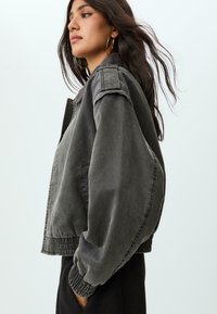 Grå denim bomberjakke med en afslappet pasform, ribbede manchetter og kant, samt skulderlapper. Glat tekstur med en let falmet finish.