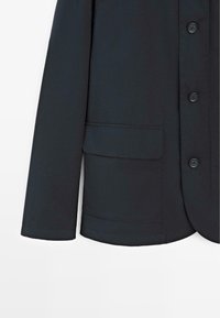 Sort jakke med knappelukning foran, lange ærmer og en enkelt påsyet lomme. Fremstillet af glat stof med en skræddersyet form og et rent finish.