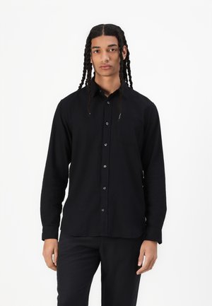 Long-sleeve black shirt made of soft fabric, featuring a collar, front buttons, and a pocket on the left chest. Paired with black trousers.