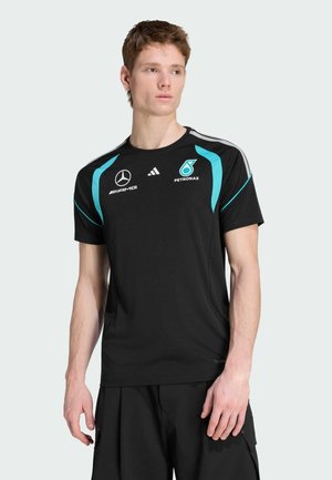 Jeune homme portant un t-shirt noir de l'équipe de course Mercedes AMG Petronas avec des accents turquoise, regardant sur le côté.