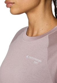 Heledus roosat värvi sportlik särk ümmarguse kaelusega, tekstuuriga kangas ja valge logo detailiga, esitleb vormitud disaini, mis sobib aktiivseks kandmiseks.
