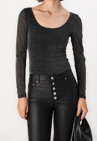 Body noir à manches longues avec un tissu brillant et texturé. Assorti avec un pantalon en simili cuir noir taille haute doté de boutons argentés.