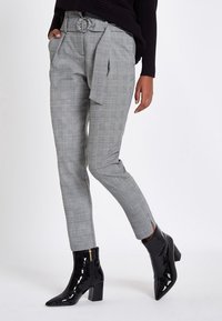 Grå rutig byxor med en knytbälte, som har sidofickor och tapered ben-design. Kombineras med svarta lackade ankelstövlar.