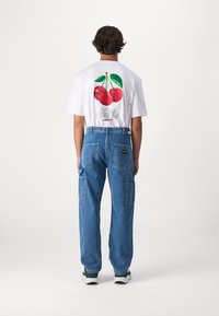 Fehér, rövid ujjú póló cseresznye grafikával és "Adidas Originals" felirattal a hátán. Kék, bő szabású farmernadrág oldalsó zsebekkel és emblémával.