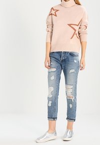 Ljust rosa polotröja med glittrande stjärnmönster, tillsammans med slitna blå jeans och glänsande silverfärgade slip-on skor.
