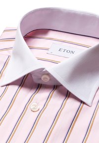 Chemise habillée avec col blanc, base rose et rayures verticales jaunes et violettes, montrant le bouton supérieur et l’étiquette de marque Eton à l’intérieur du col.