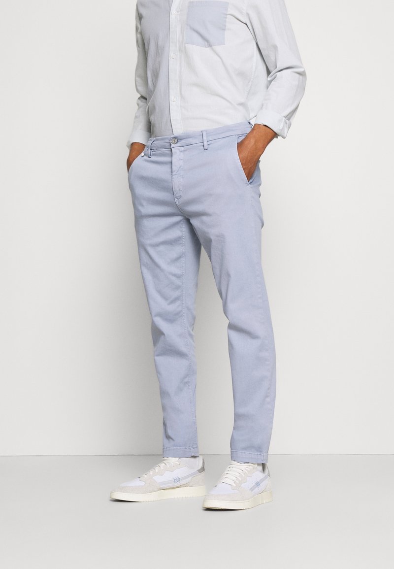 Chino azzurri chiari con vestibilità slim, dotati di tasche laterali e cintura, abbinati a sneakers bianche testurizzate e una camicia button-up azzurri chiari.