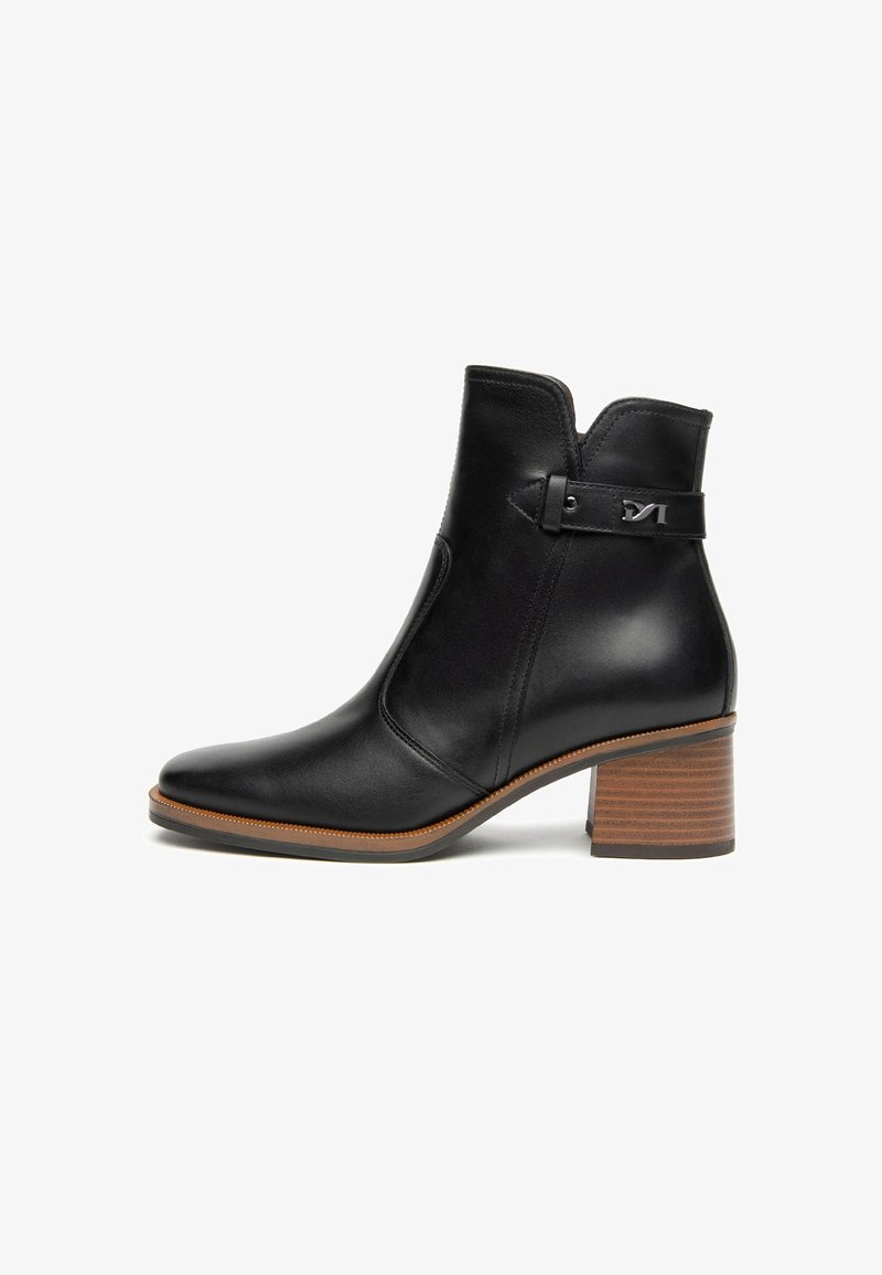 Bottine en cuir noir avec un bout pointu, panneau élastique sur le côté et un talon empilé. Elle présente une sangle et un accent métallique sur le côté.