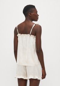 Camisola de mătase cu dantelă și bretele ajustabile, asortată cu pantaloni scurți cu tivuri dantelate. Vedere din spate.