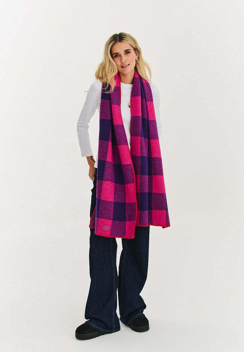 Szalik w kratę w żywych odcieniach różu i fioletu, wykonany z miękkiego materiału; ma długi, prostokątny kształt z frędzlami na końcach.