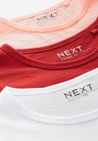 Trzy koszulki T-shirt ułożone jedna na drugiej: jedna różowa w białe paski, jedna czerwona gładka i jedna biała gładka. Wszystkie mają okrągłe dekolty i logo "NEXT".
