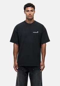 Black oversized cotton t-shirt featuring a round neckline and short sleeves, with a small graphic detail on the chest. Soft, textured fabric.