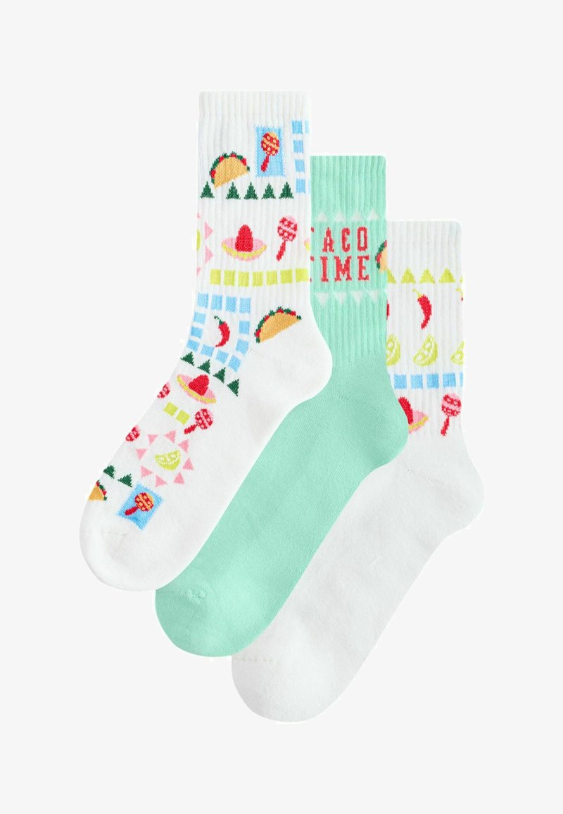 Trois chaussettes colorées, deux blanches avec des motifs de tacos, sombreros, citrons verts, piments, maracas, et une chaussette unie vert clair avec le texte "TACO TIME".