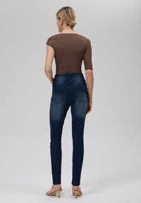 Brun stoffet topp med korte ermer, kombinert med mørk denim skinny jeans med baklommer og en glatt tekstur. Nøytrale heler.