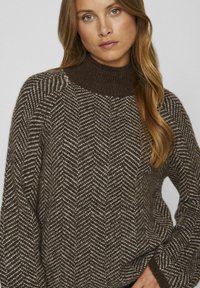 Maglione marrone a motivo con collo alto, caratterizzato da un design a spina di pesce in toni bianco e marrone scuro, con polsini a costine.