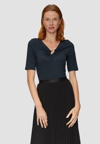 Marineblauw t-shirt met korte mouwen en een v-hals, versierd met een geplooide detail in het midden, gecombineerd met een zwarte geplooide rok en een glanzende zwarte tailleband.