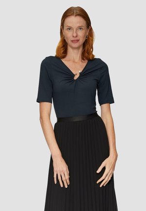 Granatowa bluzka z krótkim rękawem i dekoltem w kształcie litery V, z marszczeniem na środku, zestawiona z plisowaną czarną spódnicą i błyszczącym czarnym paskiem.