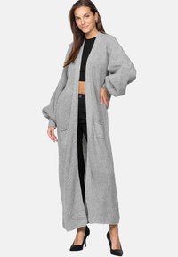 Cardigan grigio a maniche lunghe, lavorato a maglia, con vestibilità ampia, davanti aperto, due tasche frontali e una texture a coste. Presenta maniche voluminose.
