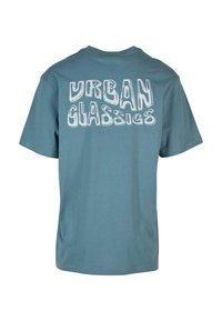 Tamsiai mėlyna trumparankovė marškinėlių su baltais užrašais "URBAN CLASSICS" drąsiame, iškreiptame šriftu ant nugaros. Lygus medvilnės audinys. Klasikinis pjūvis.
