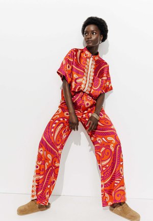 Ensemble assorti orange vif avec des motifs audacieux en rose et blanc. T-shirt à manches courtes et pantalon ample. Baskets beiges à enfiler.