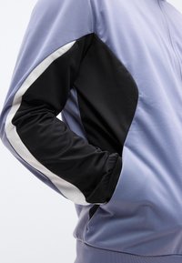 Ανοιχτό μωβ αθλητικό μπουφάν με μαύρο μανίκι και λευκή ρίγα. Λείο, υφασμάτινη υφή και εφαρμοστή σχεδίαση.