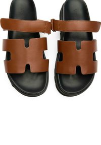 Brown leather sandals with a closed-toe design, featuring two cut-out strap sections and a black rubber sole. Adjustable strap included.
