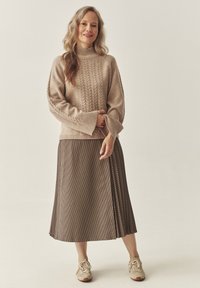 Beige koobitud sviiter kõrge kaelusega ja soonikmustriga, koos pruunika ruuduline midi-seelikuga ja neutraalsete sneakers'itega. Pehmed tekstuurid, lahtine lõige.